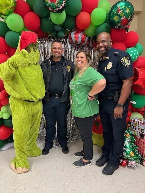 The Grinch posing with police officers and a woman at a party. 