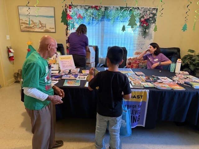 A child and an adult standing at a table with books and other items on it. 