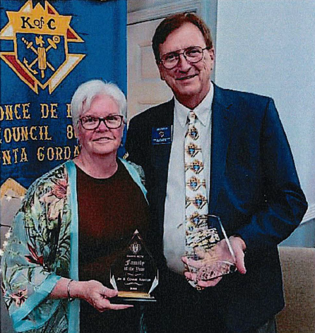 A man and a woman are standing and smiling while holding awards. 
