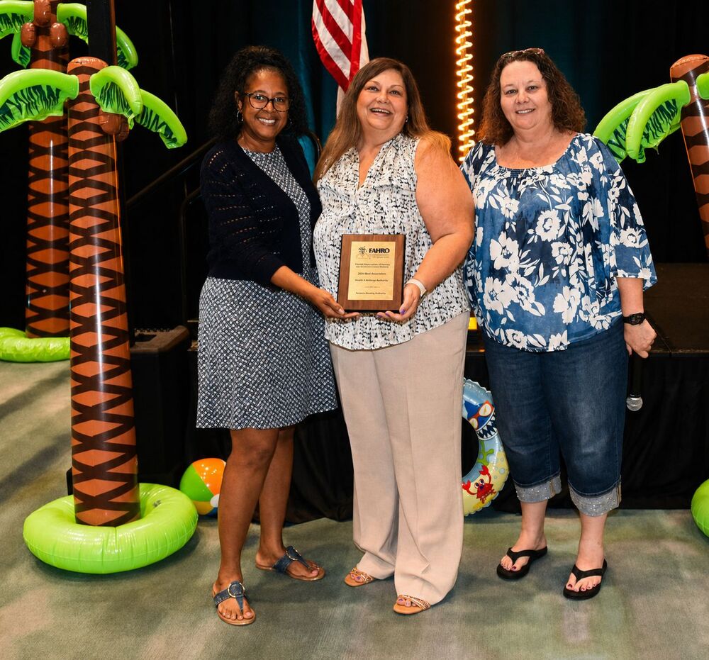 Becky-Sue stands with two other women beside her, holding an award and smiling for a photo.