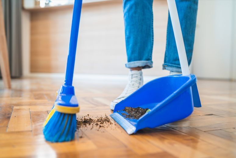 A close up of a broom sweeping dirt off of the floor and into a dustpan.