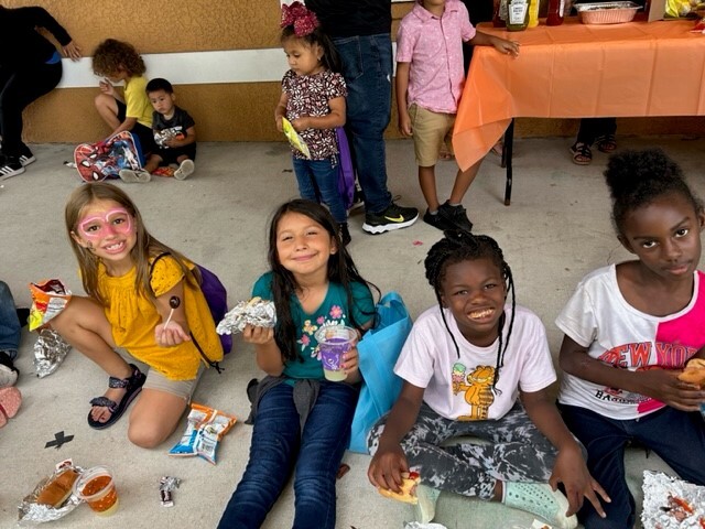 Children at the Fall Festival with their faces painted having snacks and grinning at the camera.