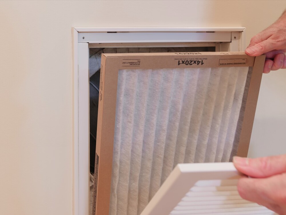 A pair of hands putting a filter into the intake for HVAC maintenance.