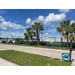 View of street, grass, trees, a chair, and the back of buildings with a fence.