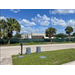 View of street, grass, trees, two trashcans, and the back of buildings with a fence.