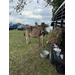  A cow standing next to a trailer with a food bucket, and some hay. 