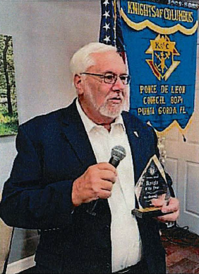 Gentleman speaking while holding an award and a microphone.