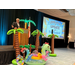  A man speaking at a podium on stage with palm tree inflatables in front of it, and the words Legislative Update with Neil Brickfield on a projector screen next to him. 